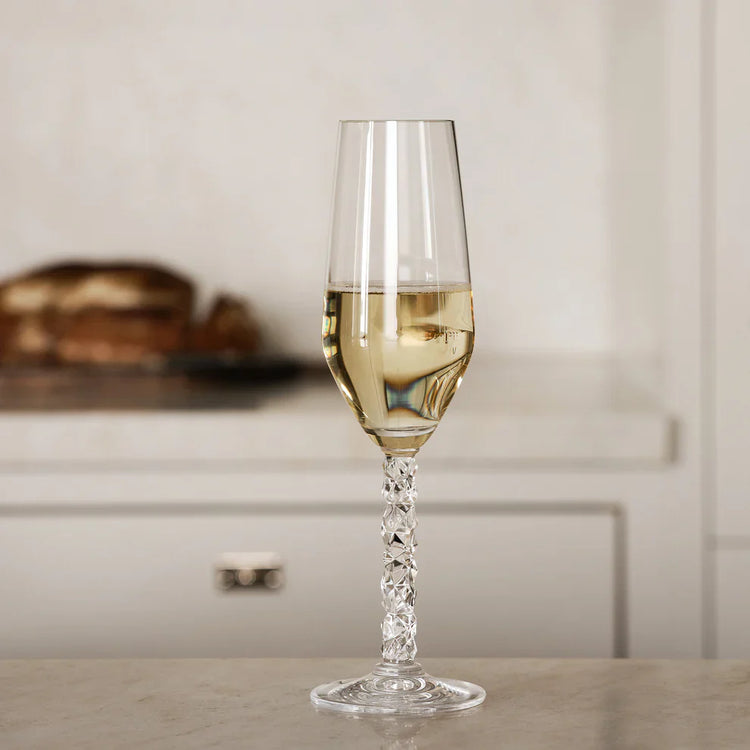 Champagne flute with a decorative stem filled with champagne on a neutral background