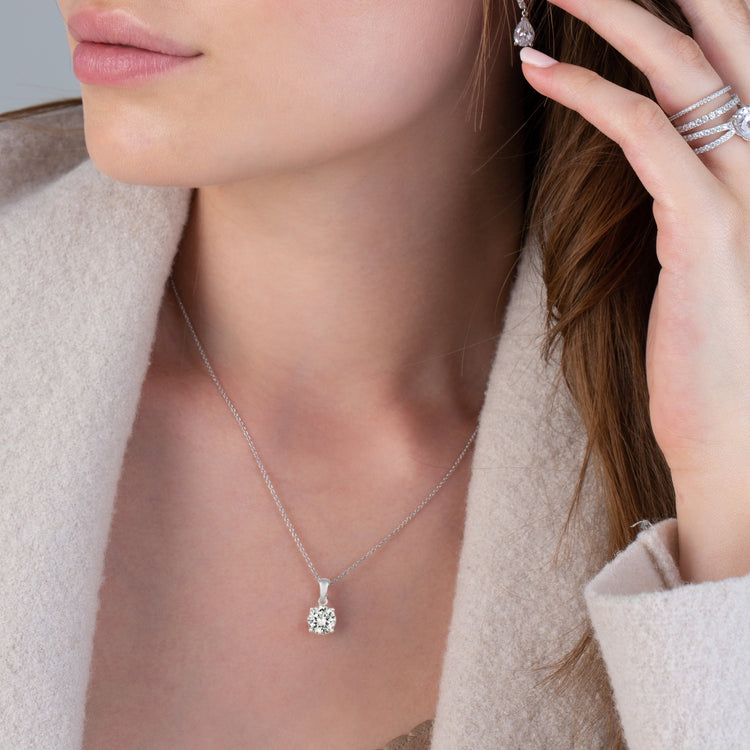 Close-up of a woman wearing a silver necklace and earrings, with a neutral background.