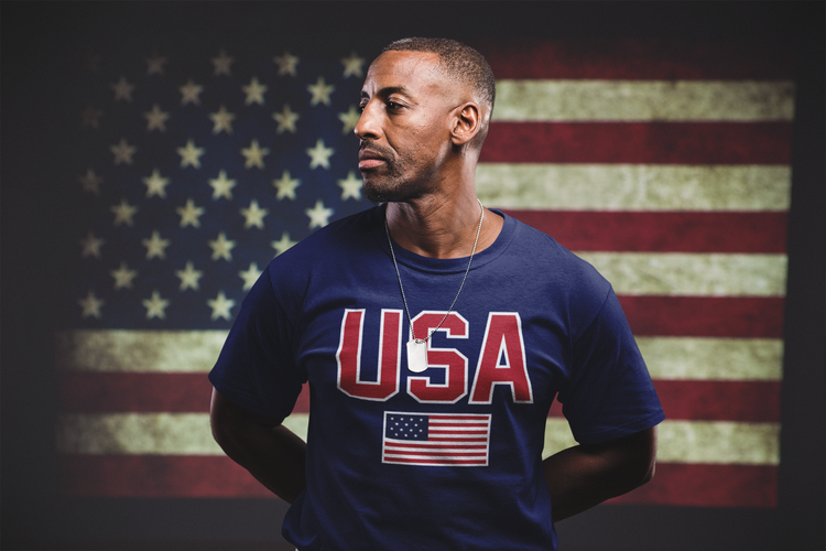 Man wearing a blue 'USA' t-shirt with an American flag in front of an American flag background