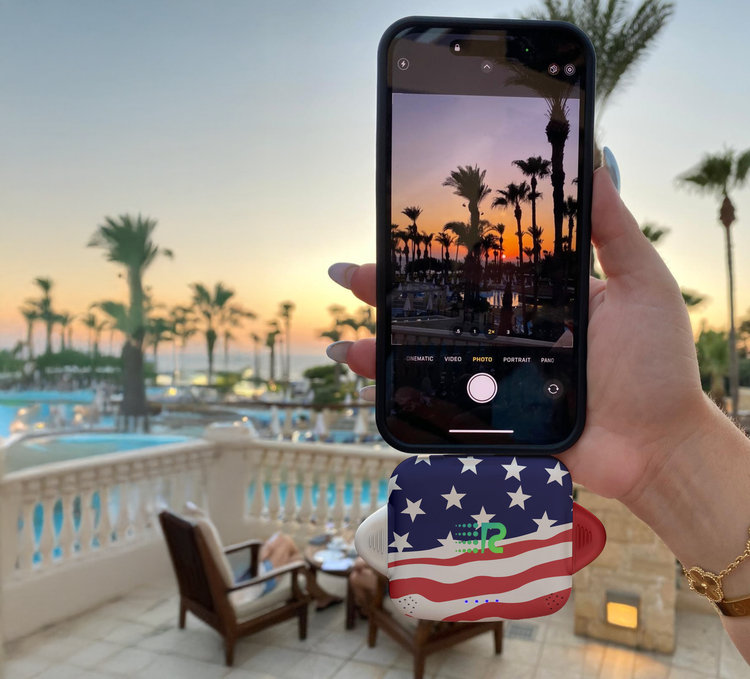 Person taking a photo of a sunset with palm trees using a phone with an American flag case.