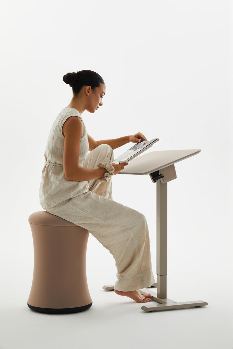 Woman sitting on a unique chair using a tablet at a standing desk.