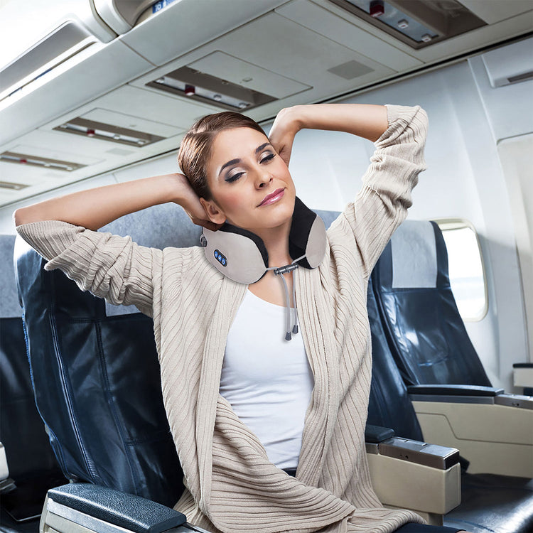 Woman sitting in an airplane seat with a neck pillow, wearing a beige cardigan.