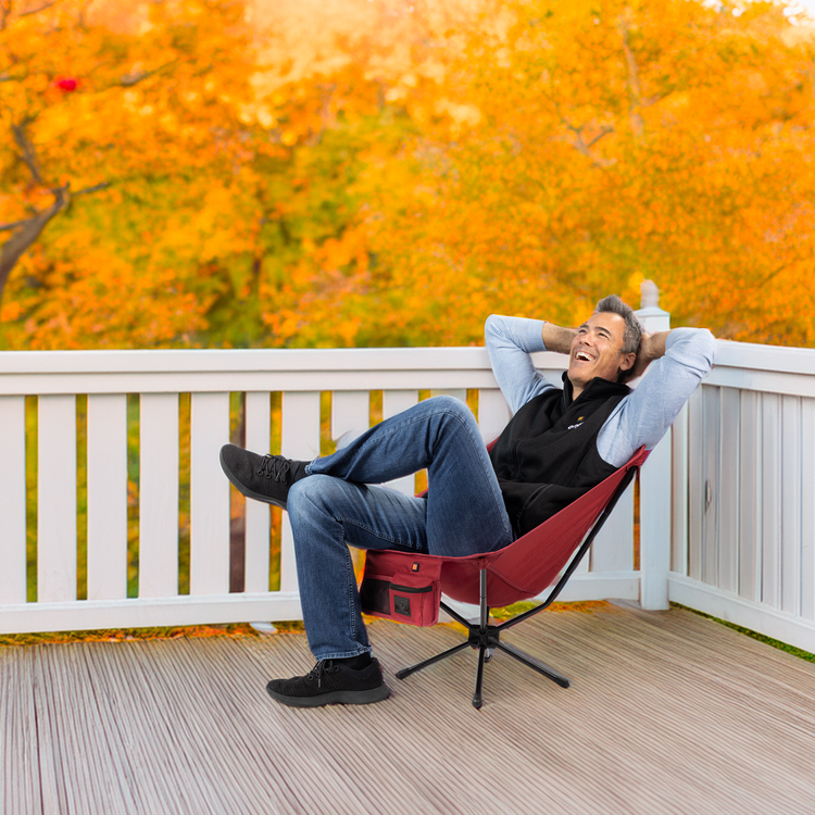 Man relaxing on a red chair on a deck with autumn trees in the background