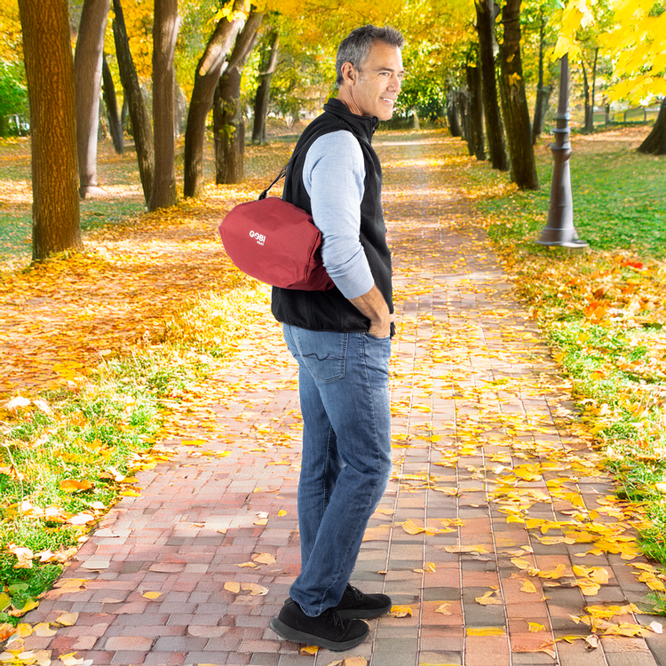 Man walking in a park with a red bag, surrounded by autumn leaves.