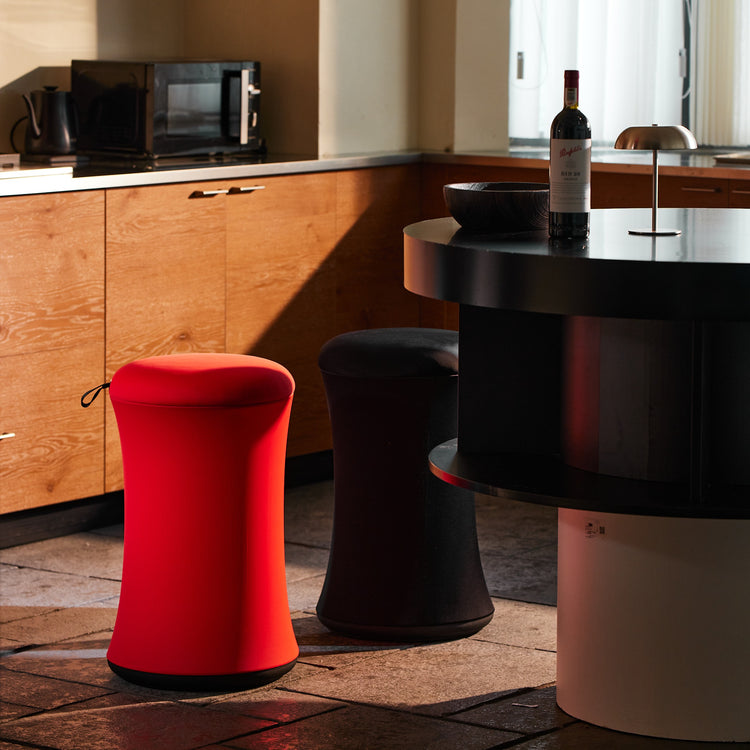 Red stool and black barstool in a kitchen setting with a bottle of wine on a counter.