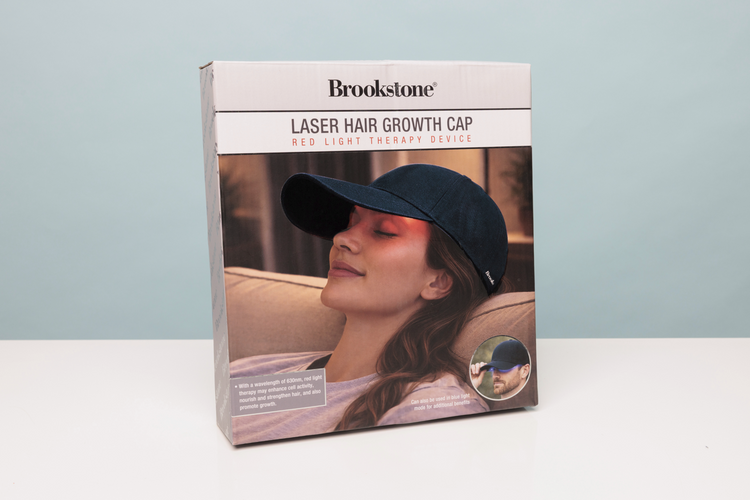 Brookstone Laser Hair Growth Cap packaging with a woman wearing the cap on a light blue background