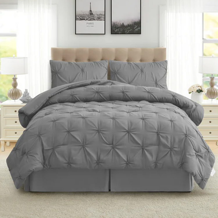 Gray comforter set on a bed in a bedroom with light-colored walls and furniture.