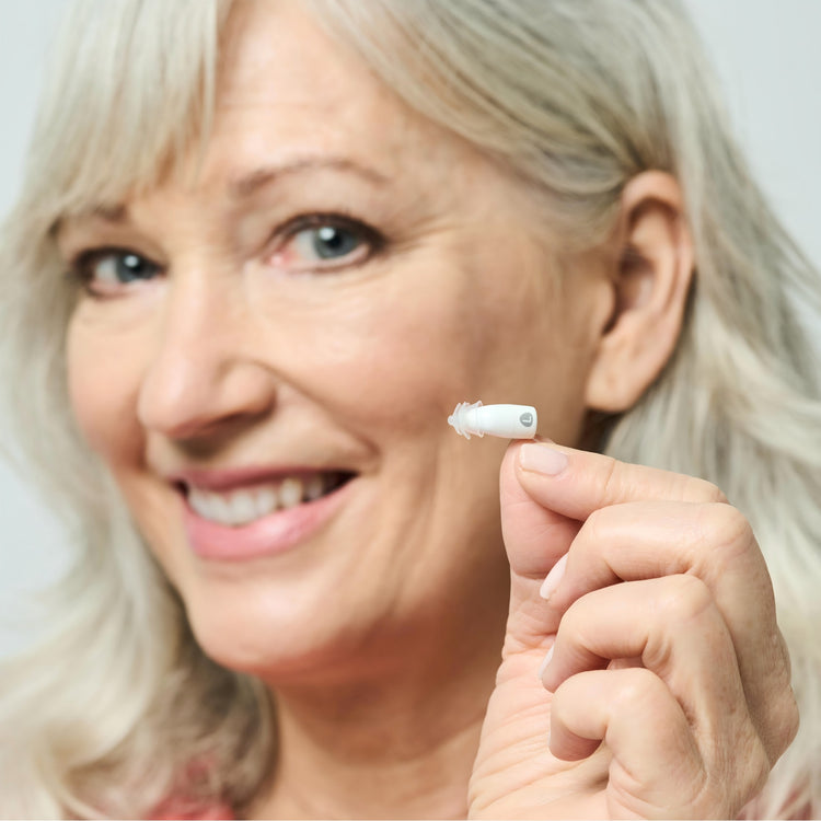 Woman holding a small white device near her ear against a light background
