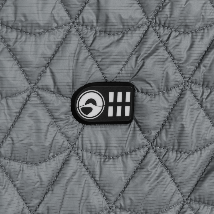 Quilted gray jacket with a logo patch on a textured fabric background