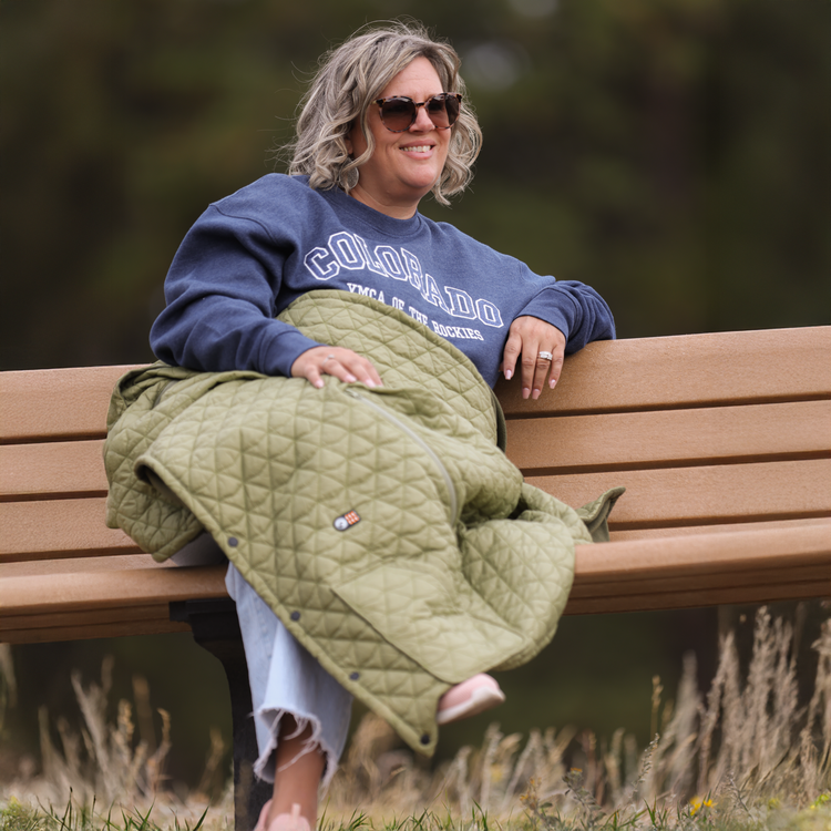 Person sitting on a bench with a green quilt, wearing a blue sweatshirt with 'Colorado' text.
