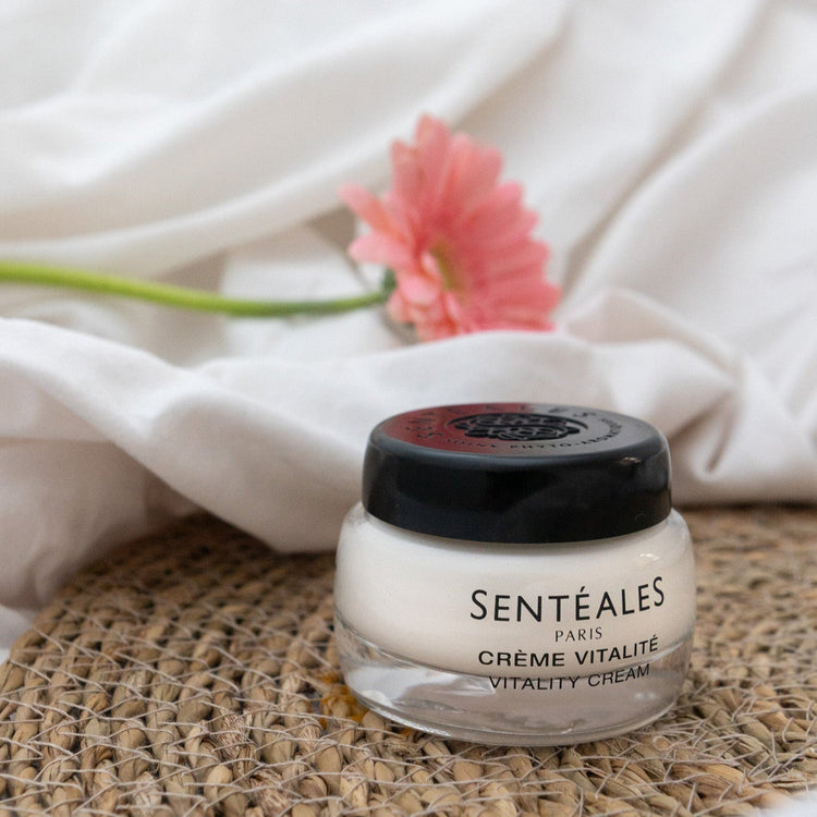 Jar of Senteaèles Paris Crème Vitalité on a woven mat with a pink flower in the background.