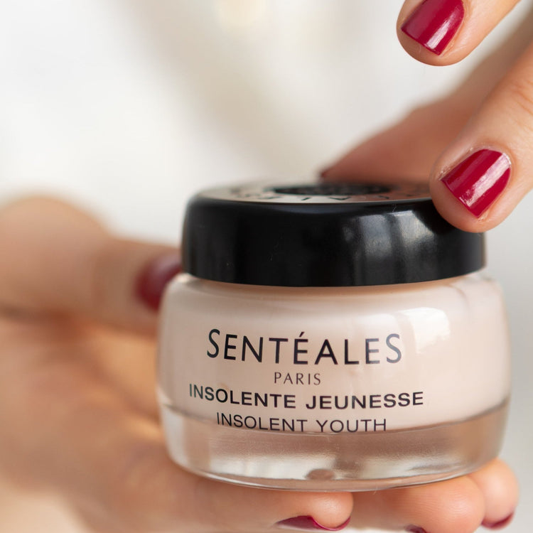 Hand holding a jar of Sentéales skincare product with a blurred background