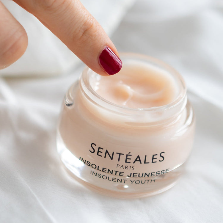 Hand holding a jar of Senteales cream with a white background