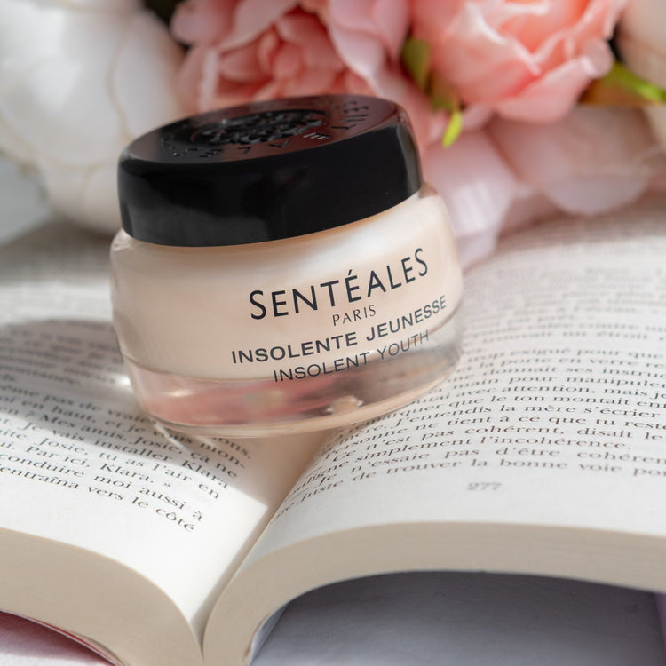 Jar of Sentéales cream on an open book with flowers in the background
