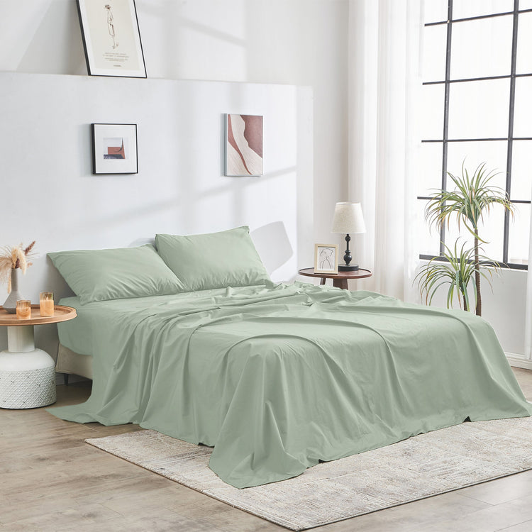 Green bedspread set on a bed in a bright bedroom with decor elements.
