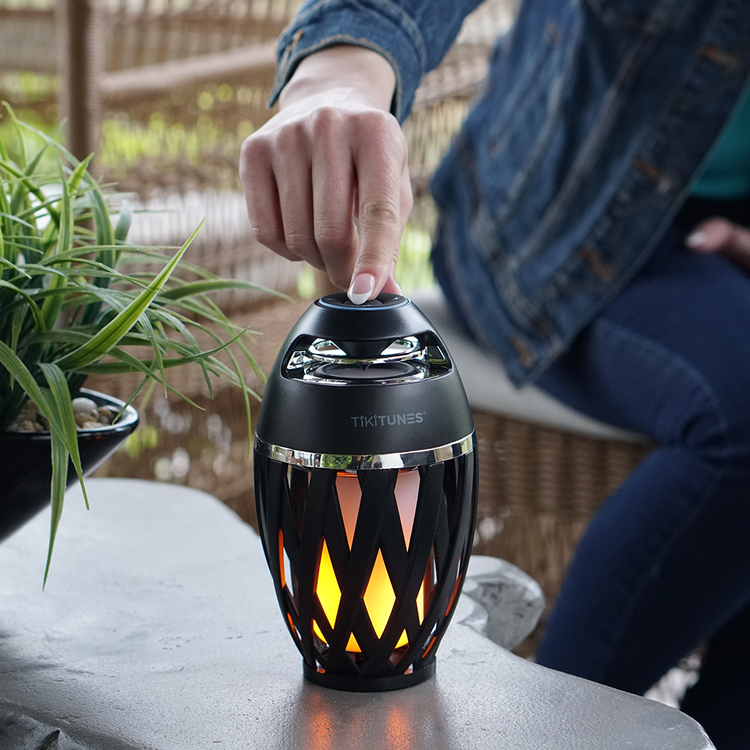 Tikkitunes outdoor speaker with decorative flame design on a table outdoors.