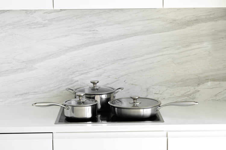Set of stainless steel cookware on a kitchen counter with a marble backsplash.