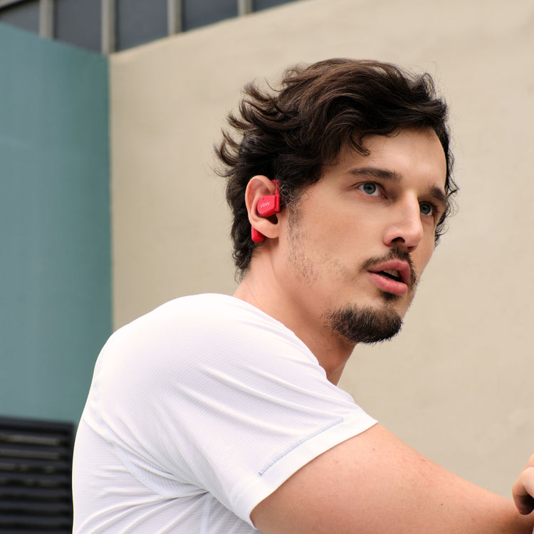 A person wearing open-ear wireless earbuds in a gym setting, drinking water from a bottle.