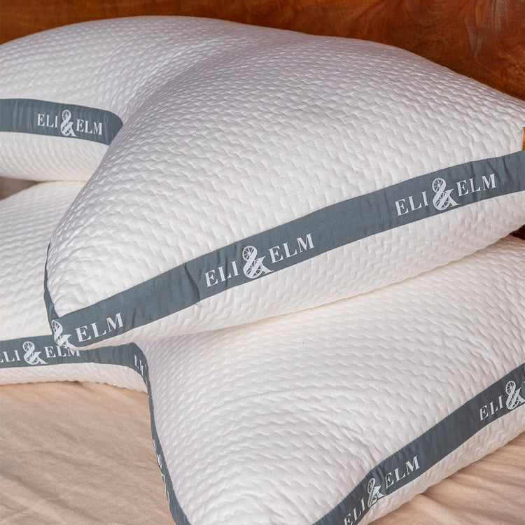 Stack of white pillows with 'ELI & ELM' branding on a wooden surface.