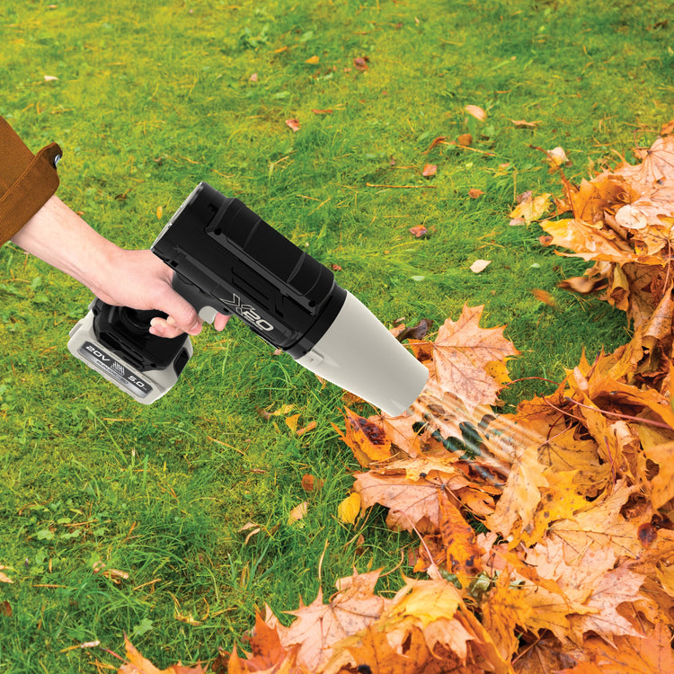 Person using a leaf blower to clear autumn leaves from a lawn
