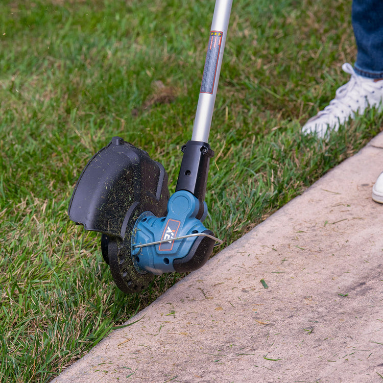 String trimmer being used to trim grass along a sidewalk