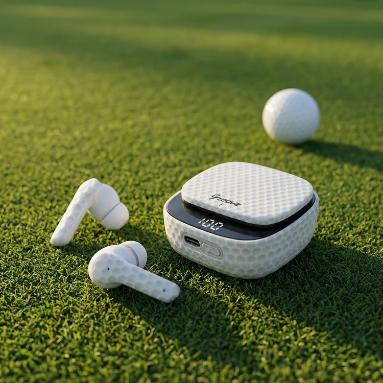 White wireless earbuds with charging case on a grassy surface with a golf ball in the background.
