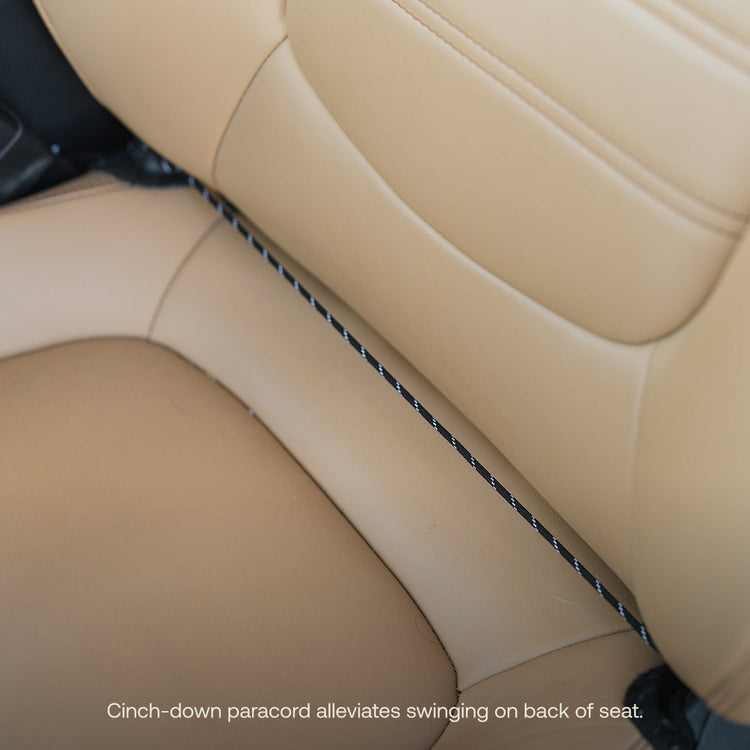 A close-up of a beige leather car seat features a black paracord with white specks running horizontally. The cord is snugly secured between seat sections, preventing swing on the Luno® Seatback Organizer. Ideal for organizing car camping essentials.