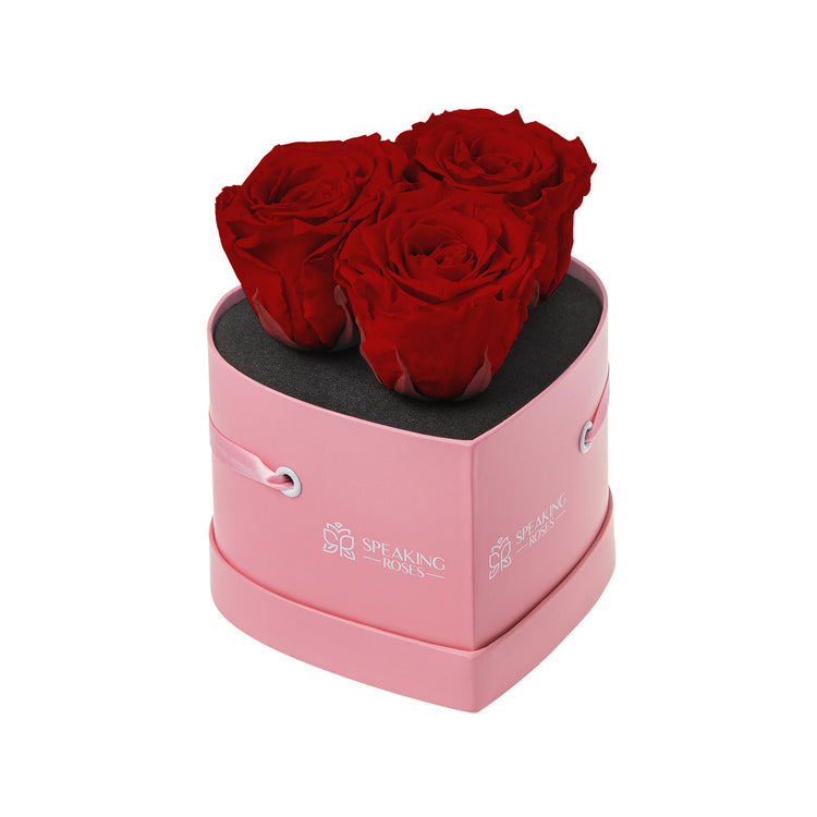 Pink heart-shaped box with three red roses on a white background