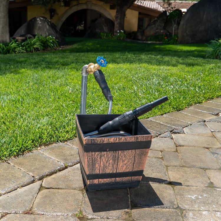 Wooden bucket with garden tools on a stone patio with grass and a building in the background