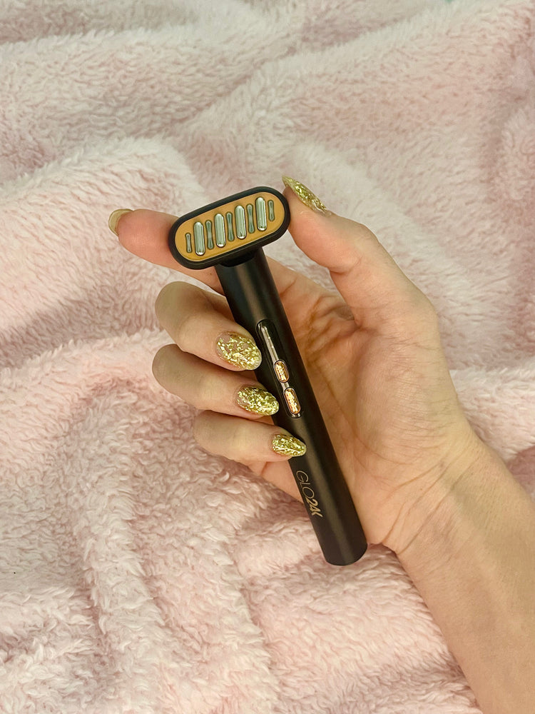 Hand holding a black and gold hair removal device against a pink textured background