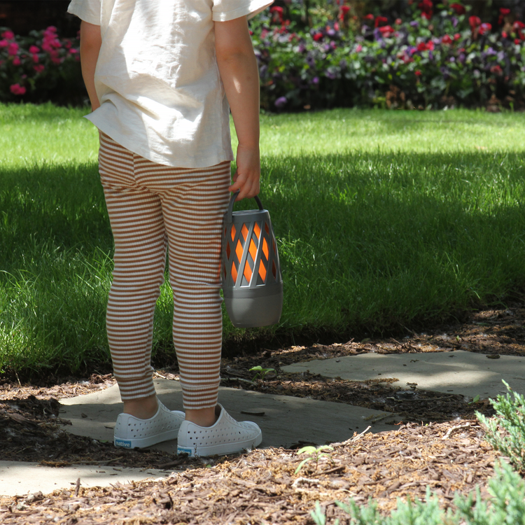 Person holding a lantern outdoors with green grass and flowers in the background