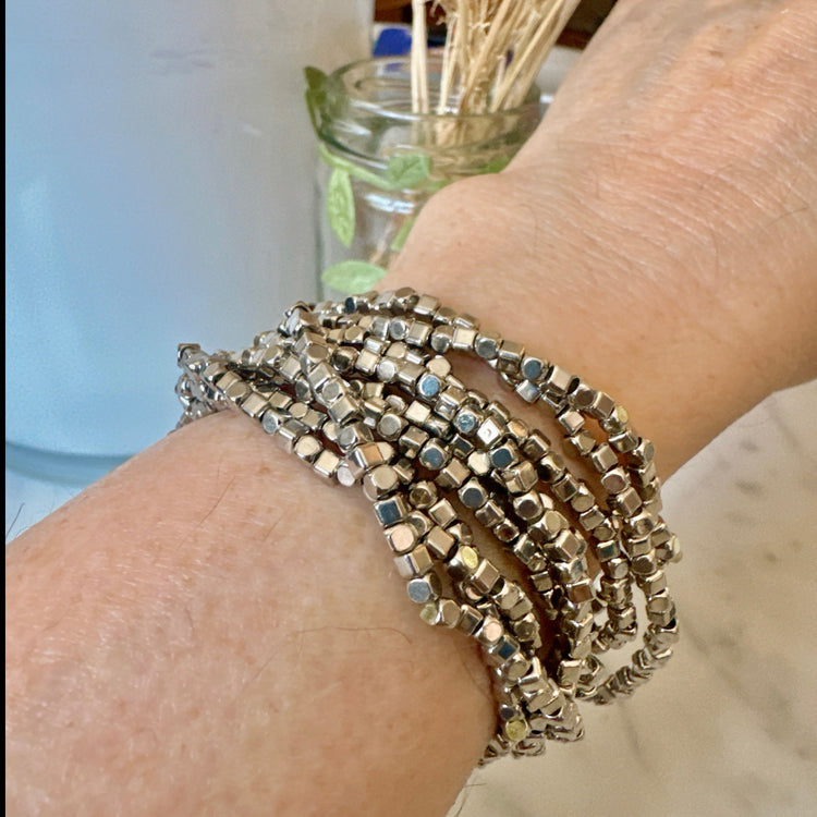 A person's wrist wearing multiple silver stretch bracelets with a focus on the jewelry.