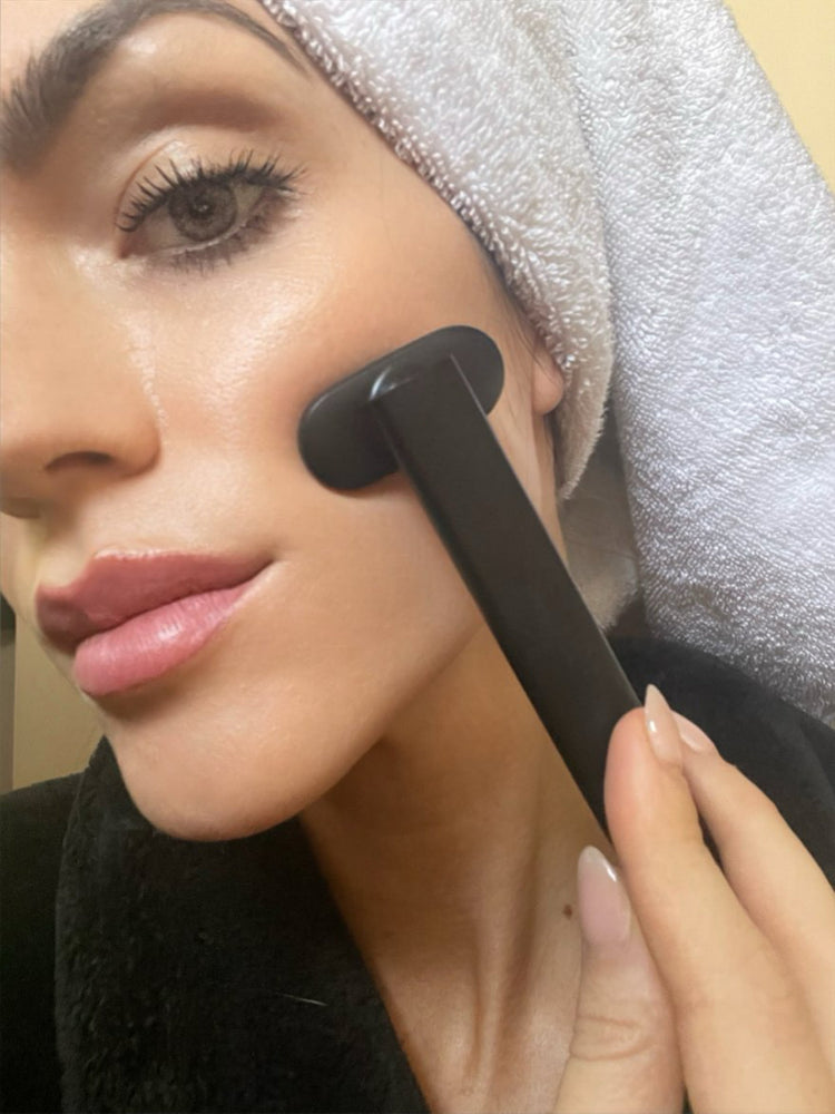 Woman using a black device on her face with a towel on her head
