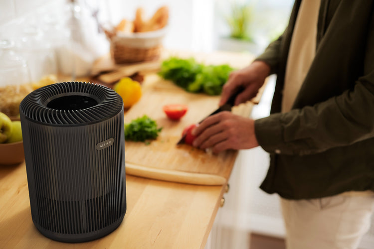 Black air purifier on a kitchen counter with a person chopping vegetables in the background