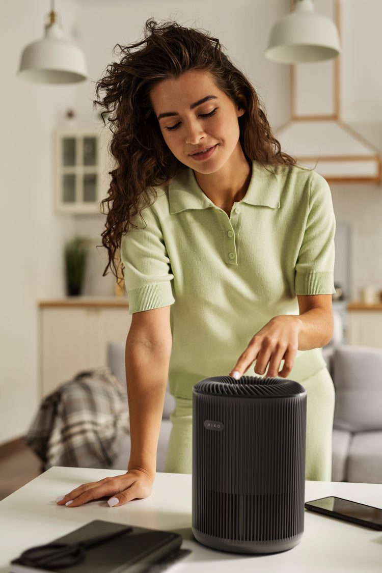 Woman interacting with a black air purifier on a table in a modern living room.