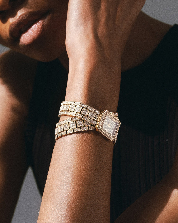 A person in a sleeveless black top poses with the JBW Watches Arc Double | J6390C, featuring a gold square case, double-wrap band, and crystal-studded bezel—both encrusted with sparkling diamonds for an elegant look.