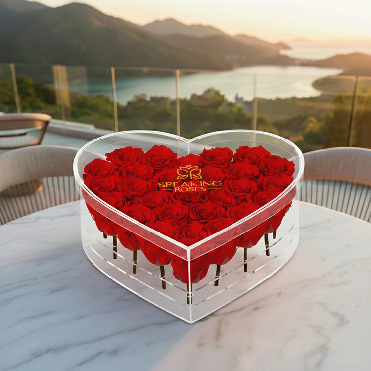 Heart-shaped box of red roses with 'Spearling Roses' branding on a marble table with a scenic background.