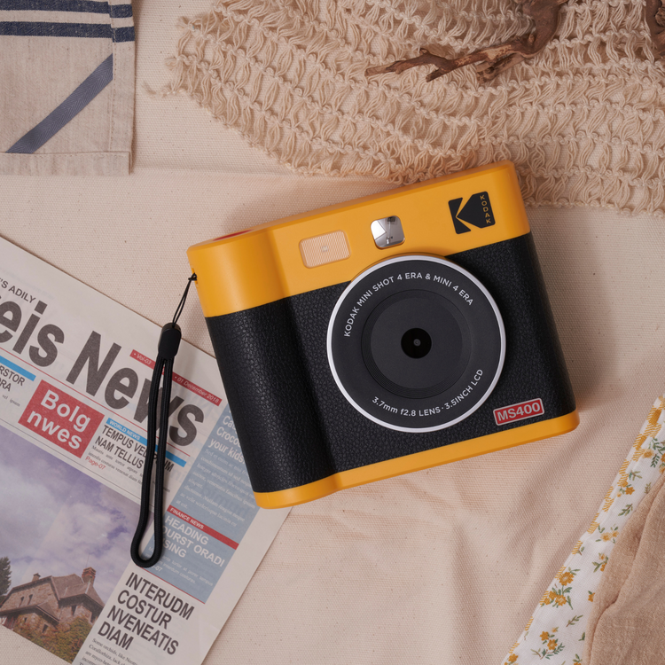 Yellow and black Kodak camera on a surface with newspaper and fabric in the background
