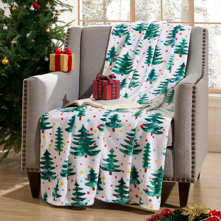 Christmas-themed blanket with trees and polka dots draped over a chair next to a decorated Christmas tree.