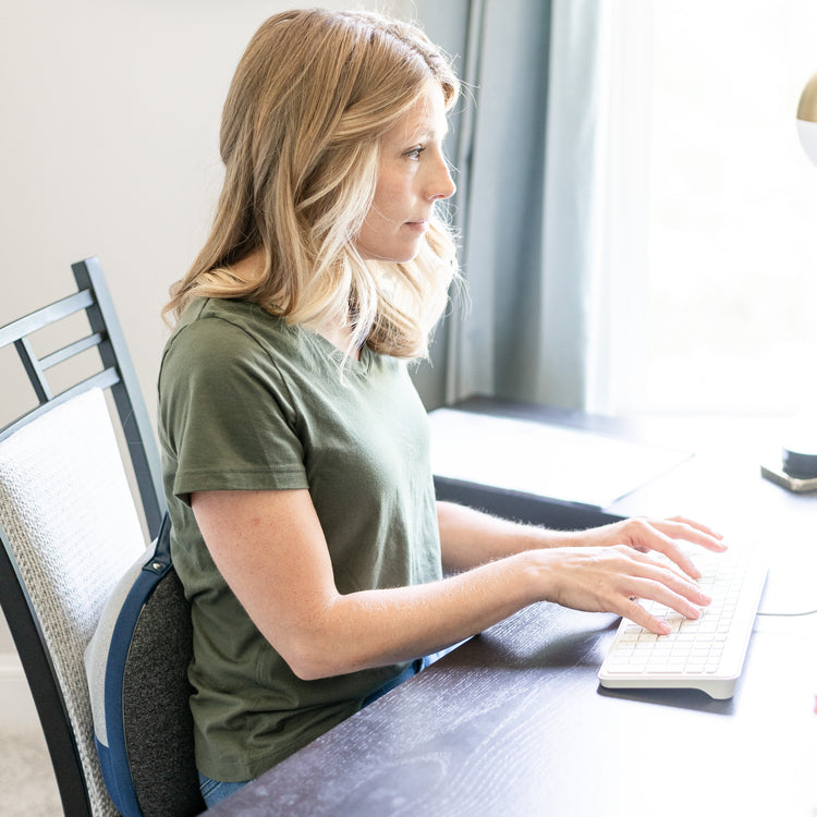 Woman typing on a keyboard at a desk in a bright room.