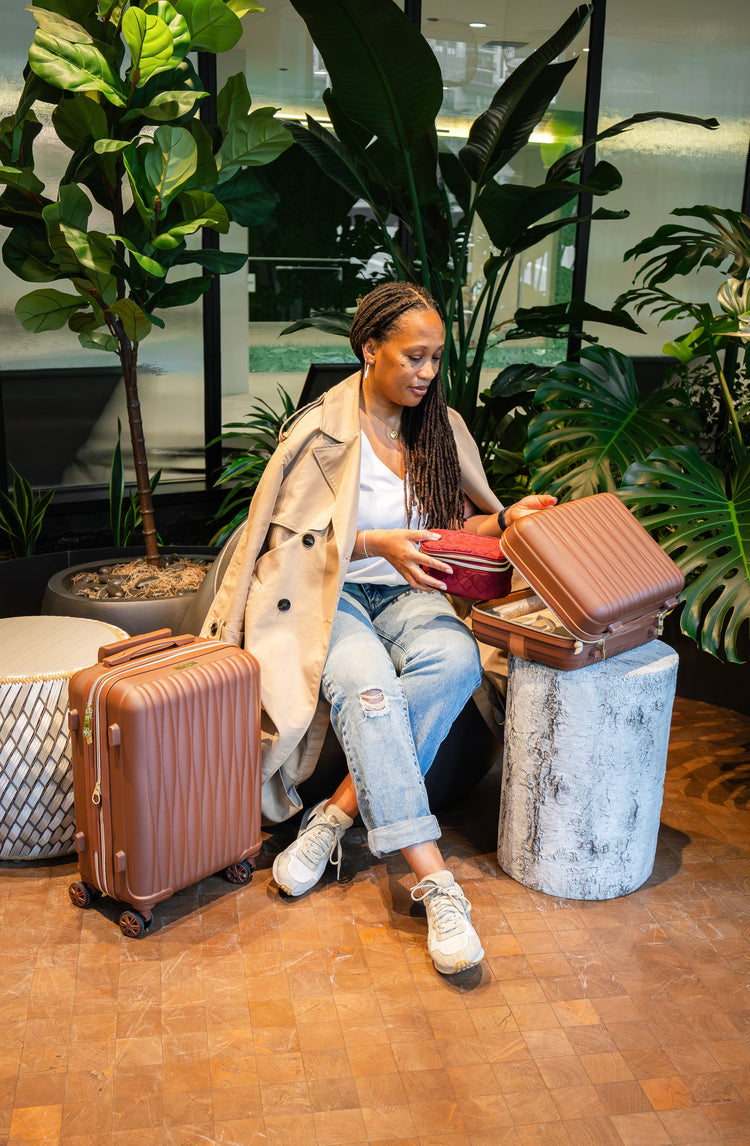 Woman sitting with a suitcase and open bag in an indoor setting with plants.