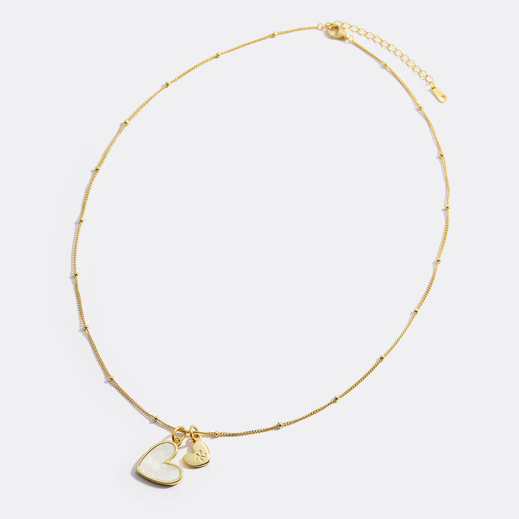 Gold necklace with heart-shaped pendant on a light gray background