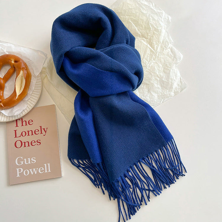 Blue scarf with fringes on a white surface next to a book and a pretzel.
