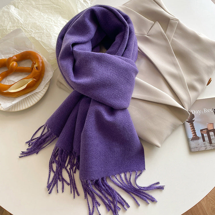 Purple scarf with tassels on a white surface with a pretzel and magazine.