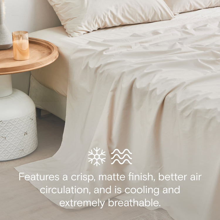 Beige bedding set on a bed with a side table and candle in a minimalistic room.