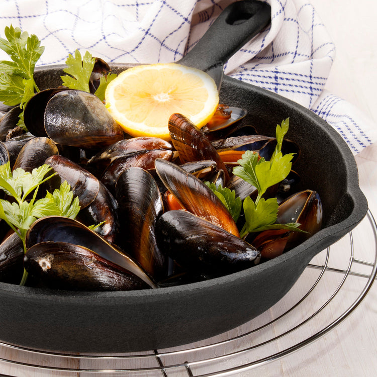 Mussels in a black skillet with lemon and herbs on a checkered cloth background