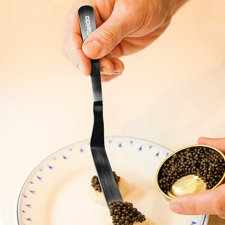 Person using a caviar spoon to serve caviar from a small dish.