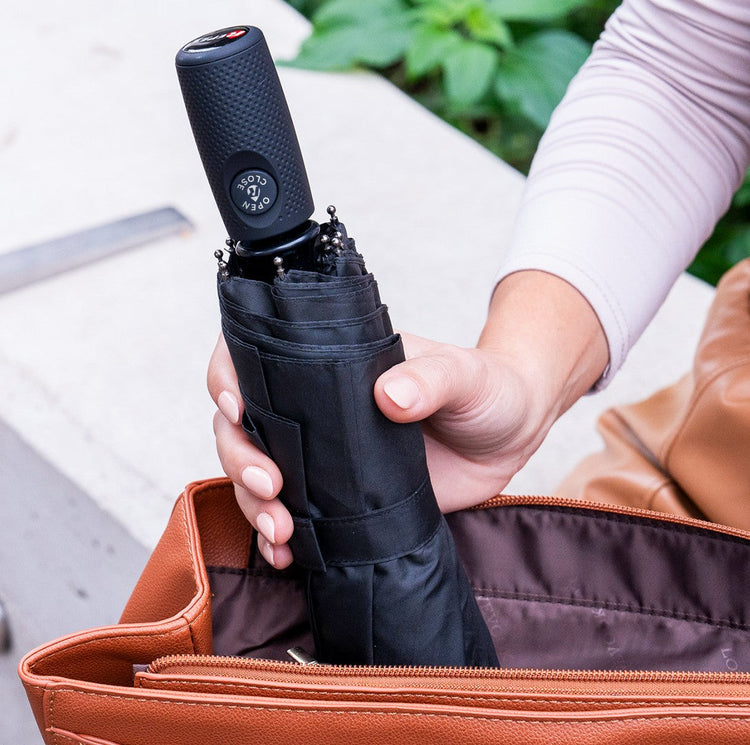 Person holding a black umbrella with a brown leather bag in the background