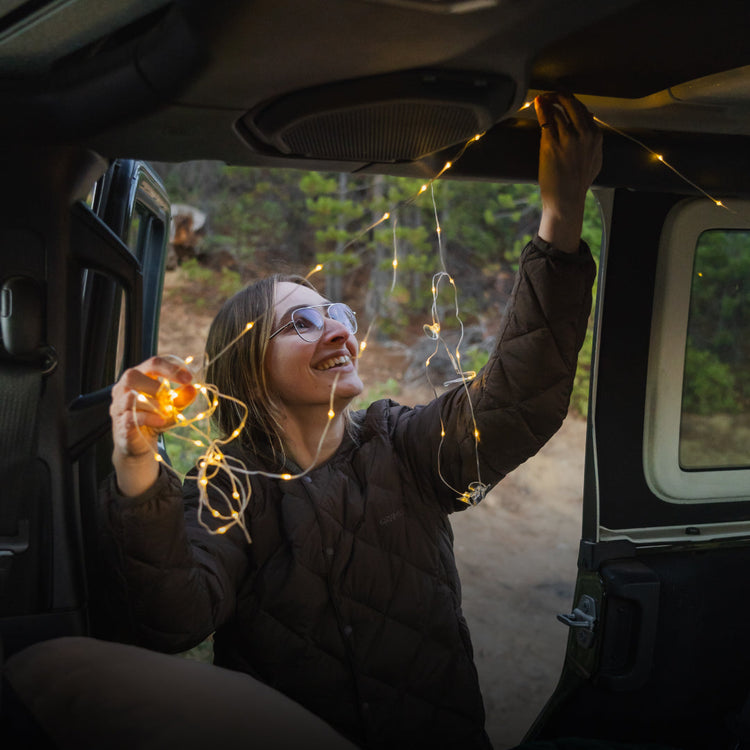 Person inside a vehicle with string lights, surrounded by nature