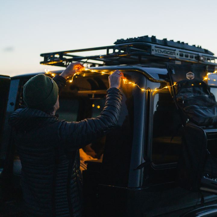 Two people decorating a car with string lights at sunset.